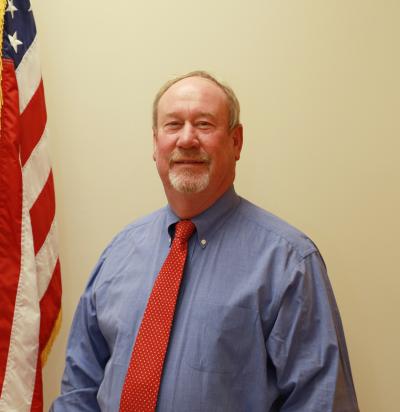 Council Member Jim Rodgers Jr. standing next to the American Flag